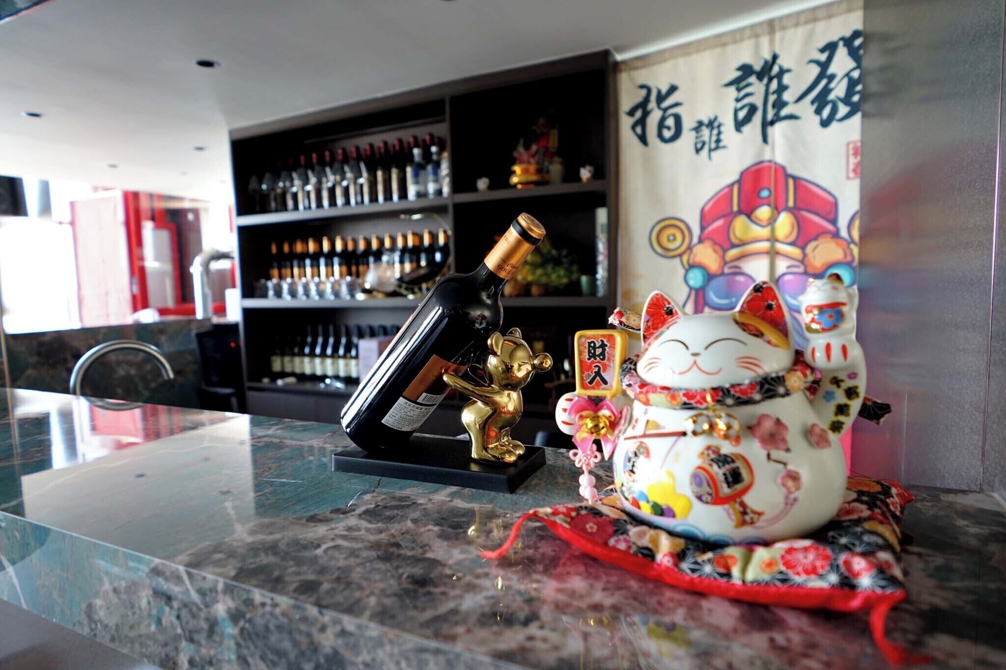 A marble countertop with a decorative ceramic cat, a gold figurine, and a bottle of wine.
