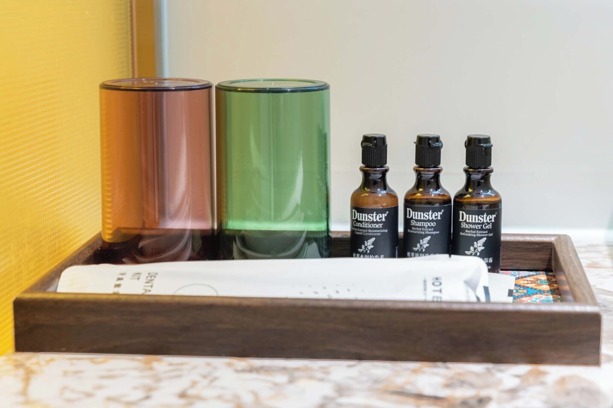 A wooden tray with a white remote control, three bottles of Dunster products, and a book on a marble surface.