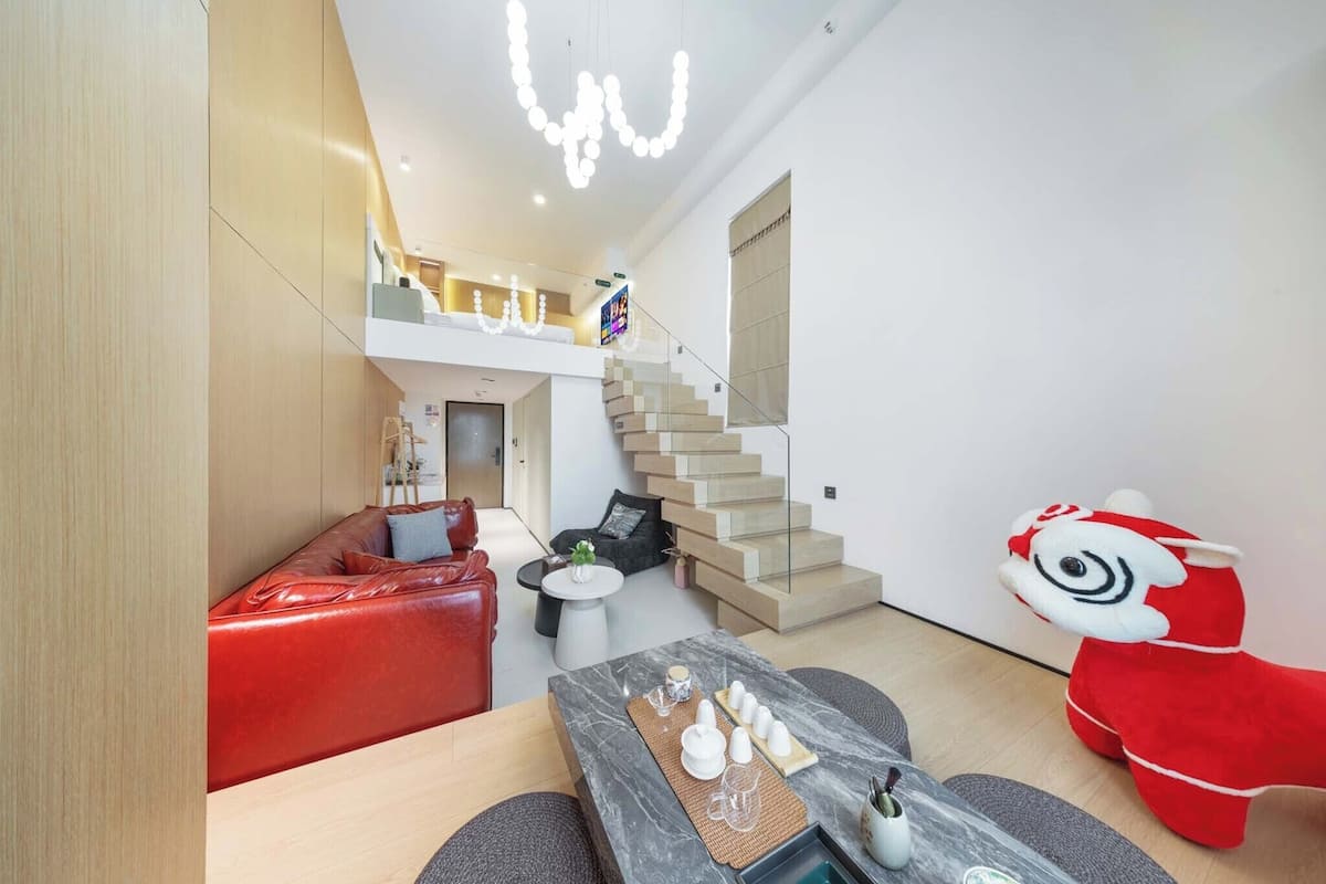 A modern interior with a staircase, a red sofa, a dining table with cups, and a plush toy.