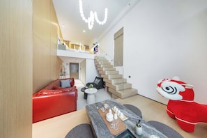 A modern interior with a staircase, a red sofa, a dining table with cups, and a plush toy.