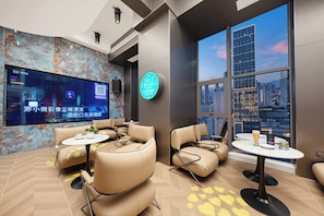 A modern lounge area with leather sofas, a large flat-screen TV, and a city view through large windows.