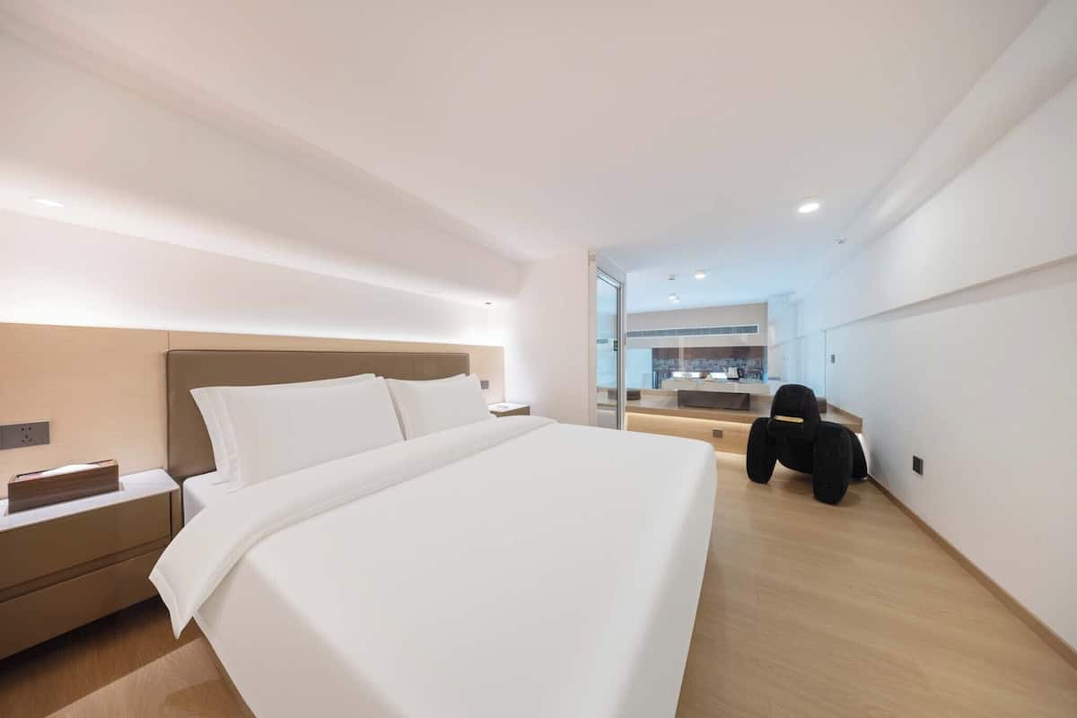 A modern hotel room with a large bed, a nightstand, a desk, and a chair.