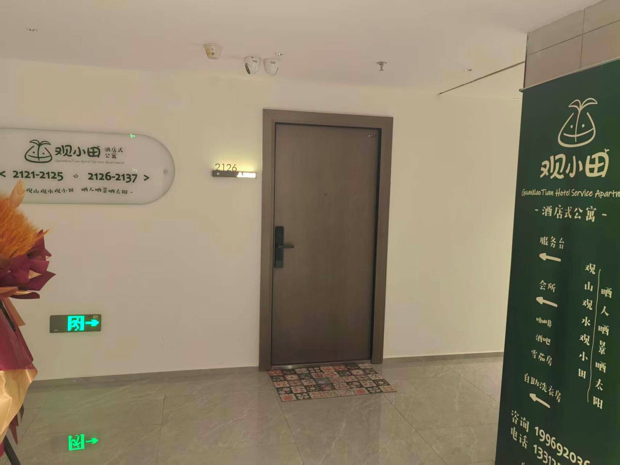 Zona de recepción de hotel con mostrador de recepción, una puerta con placa de número y señalización que indica los servicios.