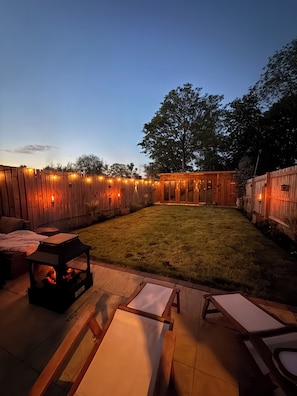 A backyard with a wooden fence, a grassy lawn, and a patio area with a table and chairs.