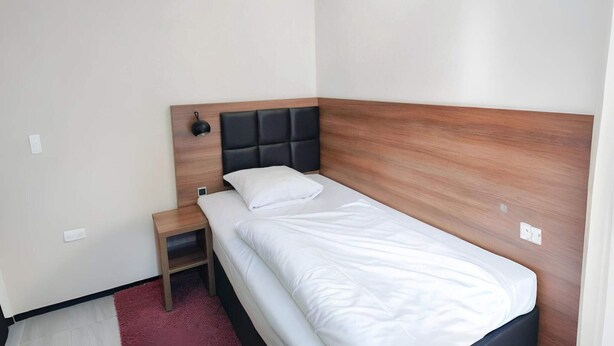 Una cama individual con cabecera de madera, una mesita de noche y una lámpara de pared.