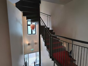 Eine Treppe mit roten Teppichstufen, schwarzen Geländern und einer hängenden Leuchte.