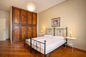 Ein Schlafzimmer mit einem Holzschrank, einem Bett mit Metallgestell, zwei Nachttischen mit Lampen sowie einer Hängeleuchte.
