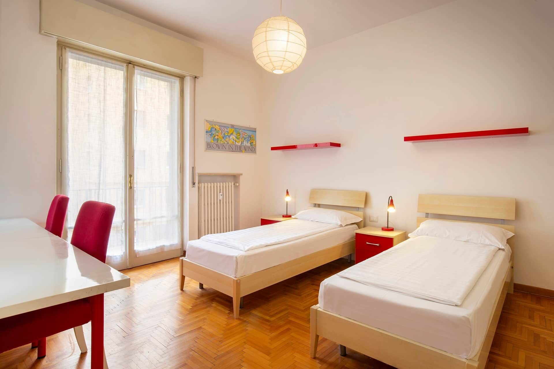 Een hotelkamer met twee bedden, een eettafel, stoelen, een radiator en een hanglamp.