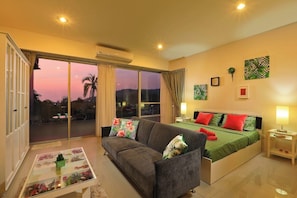 Ein Schlafzimmer mit Bett, Sofa, Nachttisch, Lampe und Blick durch das Fenster.
