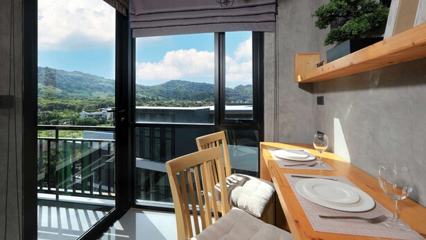 Un comedor con una mesa dispuesta para dos, vista a un paisaje montañoso a través de amplios ventanales y un balcón con barandilla.