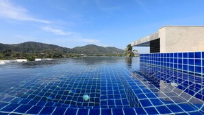 Una piscina infinita con baldosas azules, cielo despejado y un paisaje montañoso al fondo.