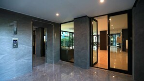 Um lobby moderno com piso de mármore, um painel de elevador digital e uma porta de vidro que dá para a área da recepção.