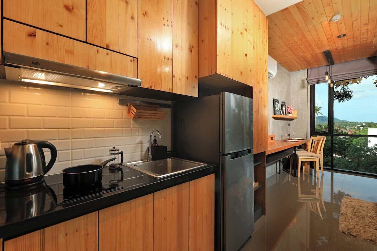 Une cuisine moderne avec des meubles en bois, un réfrigérateur en acier inoxydable et un plan de travail noir.