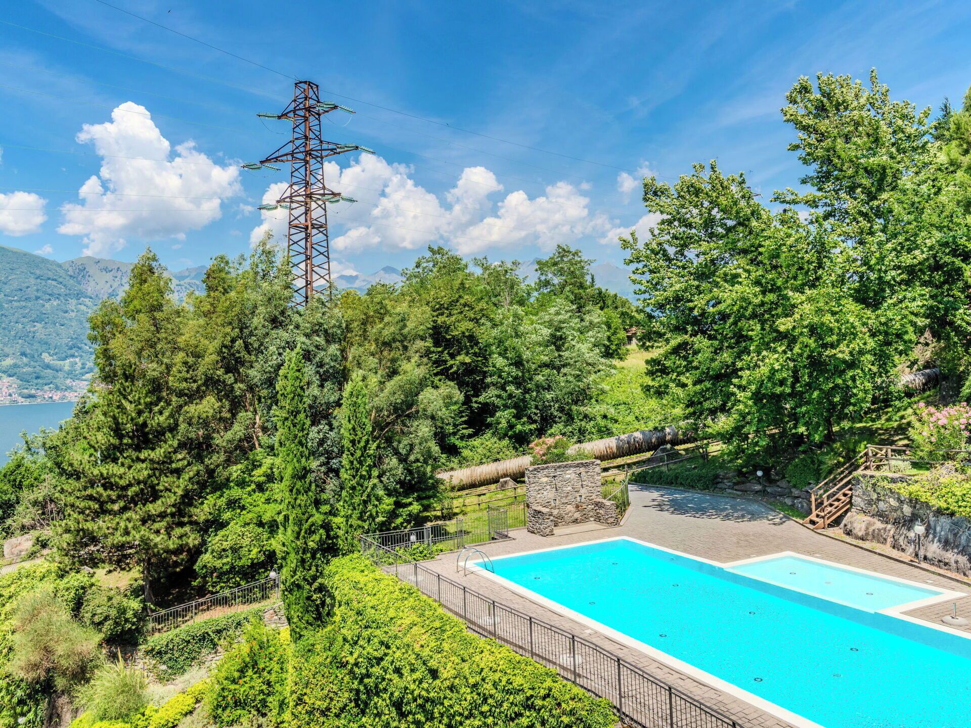 Una piscina rodeada de vegetación exuberante, una estructura de piedra y una torre de líneas eléctricas.