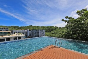Una piscina con bordo in legno, circondata da edifici moderni e vegetazione rigogliosa.