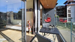 A modern balcony with a glass door, a hanging chair, and a dining table. - 2 bdr Apartment with bath NaiHarn Beach (Rawai)