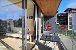 A modern balcony with a glass door, a hanging chair, and a dining table. - 2 bdr Apartment with bath NaiHarn Beach (Rawai)