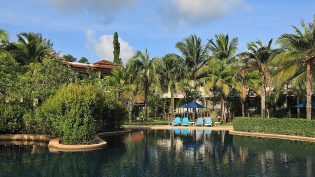 Ein Pool mit Liegestühlen, umgeben von Palmen und einem Gebäude mit rotem Dach.