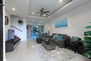 A modern living room with a sofa, coffee table, and TV stand. - Laguna Park | Bangtao Beach | 3-bedroom Townhouse (Bangtao)