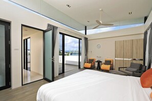 A modern hotel room with a large bed, a balcony with glass doors, a ceiling fan, and a view of the city. - Laguna Park | Bangtao Beach | 5-bedroom Pool Villa (Bangtao)
