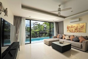A modern living room with a large flat-screen TV, a sofa, a coffee table, and a ceiling fan. - Laguna Park | Bangtao Beach | 5-bedroom Pool Villa (Bangtao)