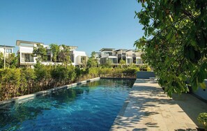 Ett modernt poolområde med en kristallklar blå pool, omgivet av moderna byggnader och frodig grönska.