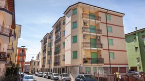 Un edificio residencial de varios pisos con balcones, una calle en su frente y automóviles estacionados.