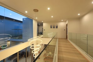 A modern interior with a glass railing, a staircase, and a view of the outside. - Zenithy | Bangtao Beach | 3-bedroom Pool Villa (Bangtao)