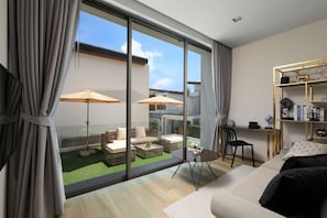 A modern living room with a large sliding glass door leading to an outdoor area, a round table with chairs, and a bookshelf with decorative items. - Zenithy | Bangtao Beach | 3-bedroom Pool Villa (Bangtao)