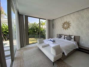 A modern bedroom with a large bed, a sofa bed, and a view of a garden through large sliding doors. - 3bdr New Modern Pool Villa Bangtao (Tambon Thep Krasatti)