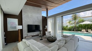 Uma sala de estar moderna com um sofá branco grande, uma televisão de tela plana e vista para a piscina.