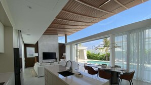 Cozinha moderna com ilha central, área de refeições com cadeiras, televisão e vista para a piscina.