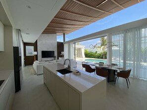 A modern kitchen with a central island, dining area with chairs, a TV, and a pool view. - 3bdr New Modern Pool Villa Bangtao (Tambon Thep Krasatti)