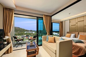 A modern hotel room with a sofa, a bed, a small table, and a balcony with a view of the city. - 1BR Sea View Apartment Surin Beach | CapitalPro (Tambon Choeng Thale)