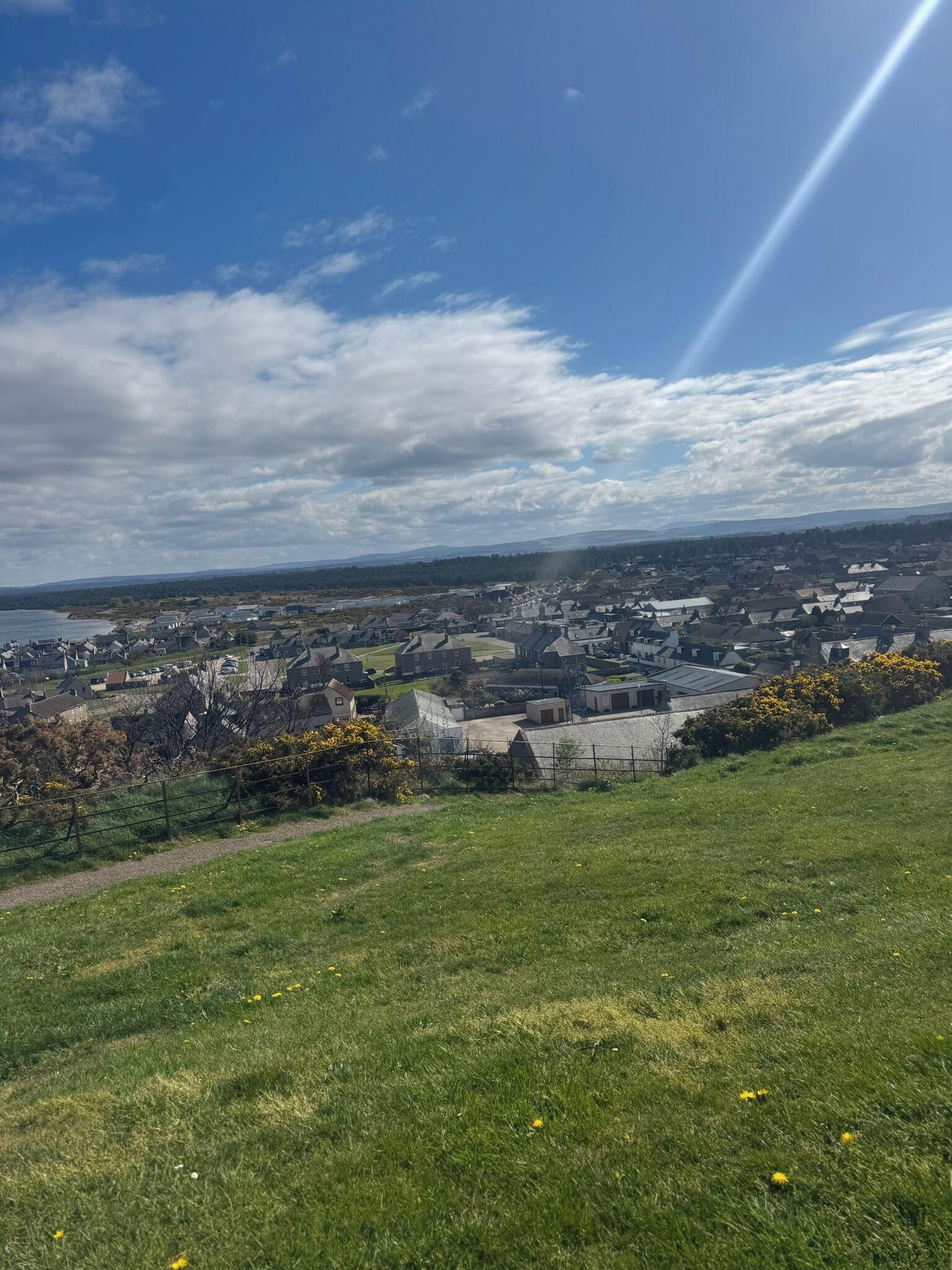 A panoramic view of a coastal town with a mix of residential and commercial buildings, a clear sky, and a distant body of water.