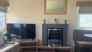 A living room with a flat-screen TV, a fireplace, a sofa, and a window. - Cabin Sleeps 4 With Wifi (Lossiemouth)