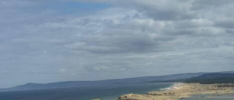 Un paisaje costero con playa, dunas cubiertas de hierba y cielo despejado.
