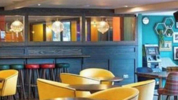 A restaurant with yellow chairs and tables, a bar area, and a blue wall with hexagonal patterns. - Cabin Sleeps 4 With Wifi (Lossiemouth)