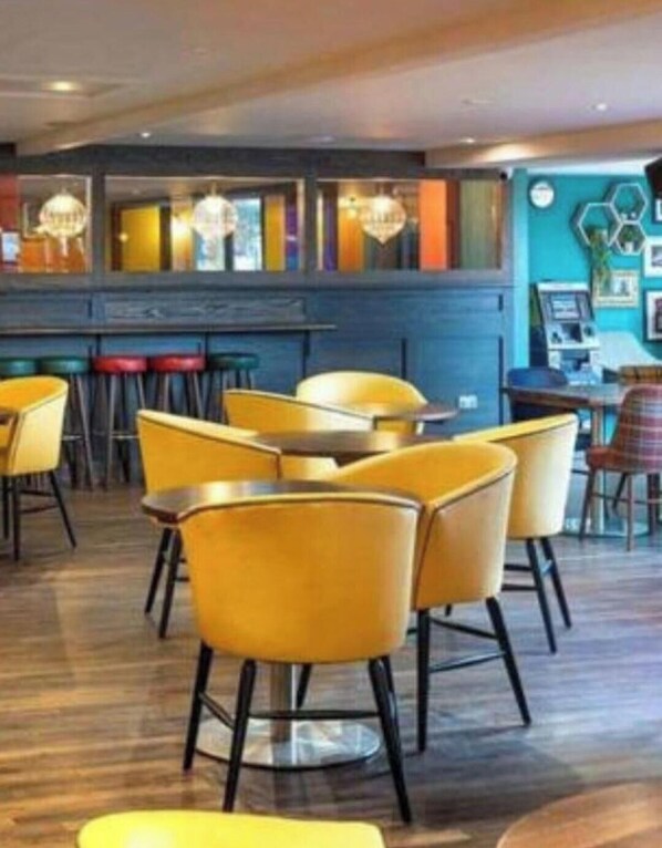 A restaurant with yellow chairs and tables, a bar area, and a blue wall with hexagonal patterns.