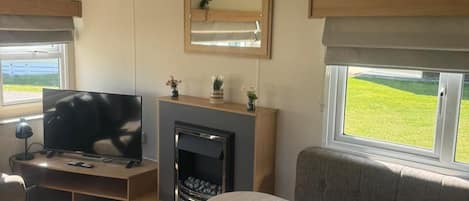 A modern RV interior with a flat-screen TV, a fireplace, and a dining area.