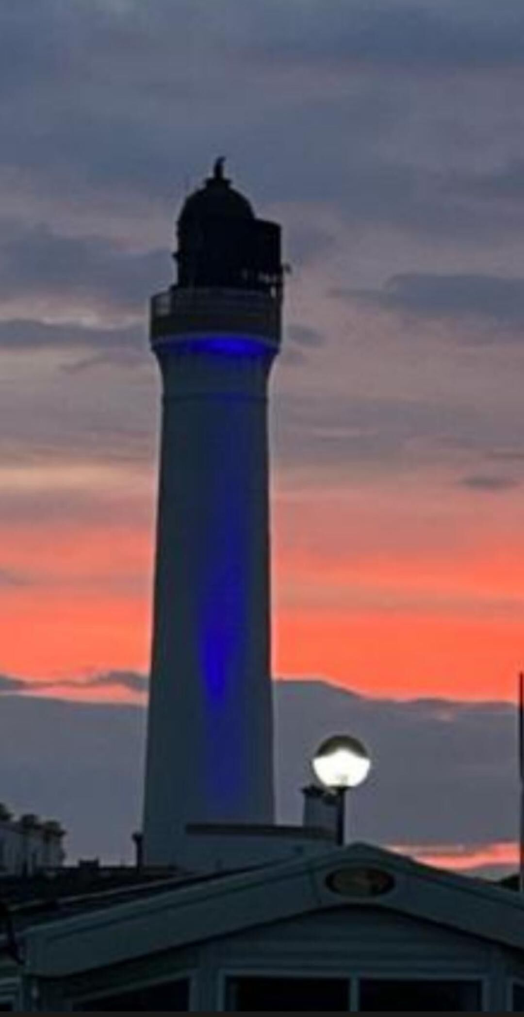 Een vuurtoren met een blauw licht bovenop, tegen een ondergaande zon.