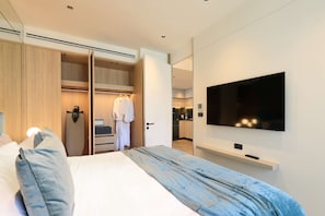 A hotel room with a bed, a TV, a wardrobe, and a kitchenette. - New 1bdr Apartment near Layan Beach (Choeng Thale)