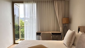 A bedroom with a bed, a desk, a chair, a lamp, and a view through a window. - 1 bdr Mountain View Apartment 50 m from Beach (Choeng Thale)