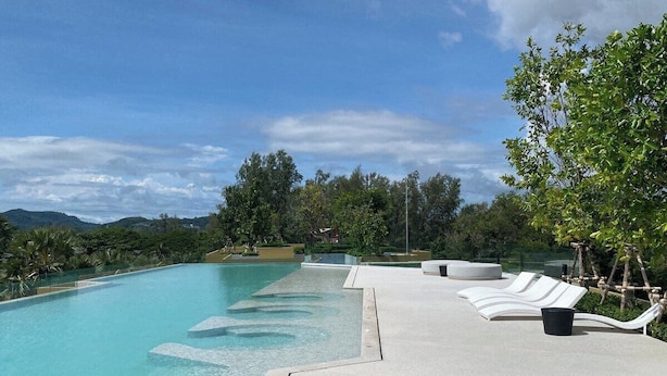 A swimming pool with clear water, surrounded by a concrete deck with lounge chairs and a view of the mountains. - 1 bdr Mountain View Apartment 50 m from Beach (Choeng Thale)