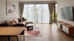 A modern living room with a sofa, coffee table, TV, and a dining area. - 1 bdr Mountain View Apartment 50 m from Beach (Choeng Thale)