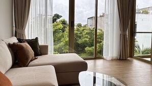 A modern living room with a sofa, a glass coffee table, and large windows with curtains. - 1 bdr Mountain View Apartment 50 m from Beach (Choeng Thale)
