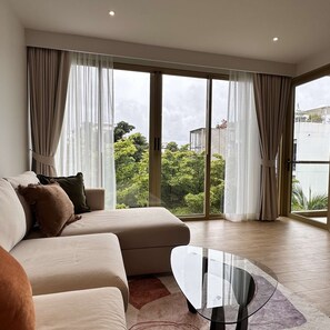 A modern living room with a sofa, a glass coffee table, and large windows with curtains. - 1 bdr Mountain View Apartment 50 m from Beach (Choeng Thale)