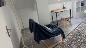 Una stanza con un letto, una scrivania, una sedia, un termosifone, un lucernario e un tappeto decorato.