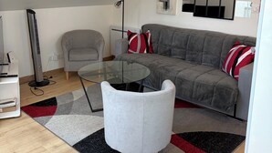 Un soggiorno moderno con un tavolino in vetro, un divano grigio e cuscini rossi e bianchi. Si nota una lampada da terra e un termosifone verticale.