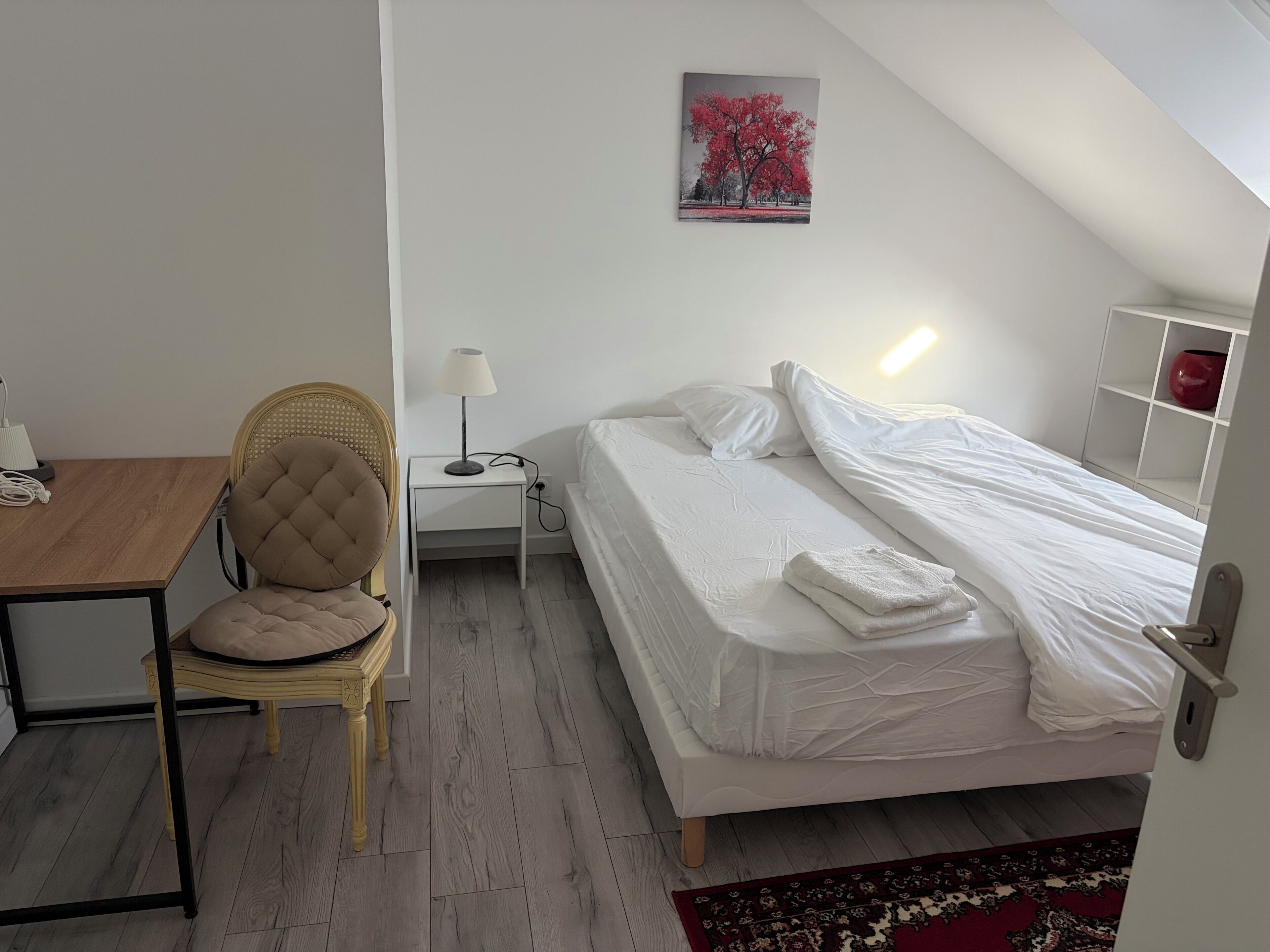Quarto com cama, cadeira, mesa de cabeceira com abajur e um quadro na parede.
